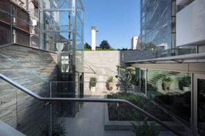 Un bâtiment moderne doté d’une façade en verre, d’un escalier et d’un petit jardin agrémenté de plantes en pot.