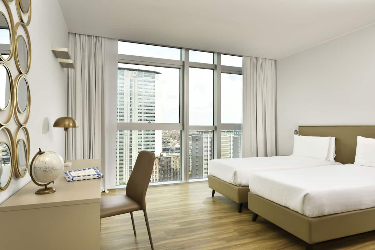 Una habitación de hotel con un ventanal grande, un escritorio con un globo terráqueo, una silla y una cama.