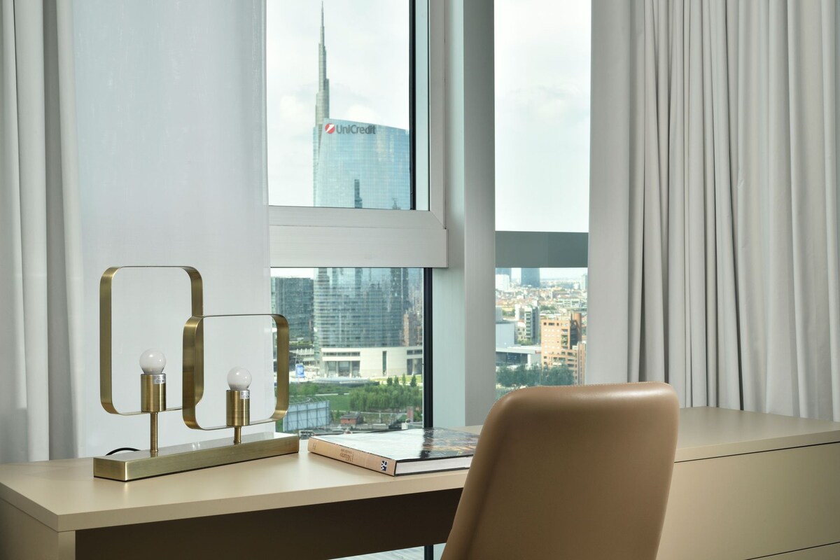 A modern desk with a lamp, a book, and a view of a cityscape through a window.