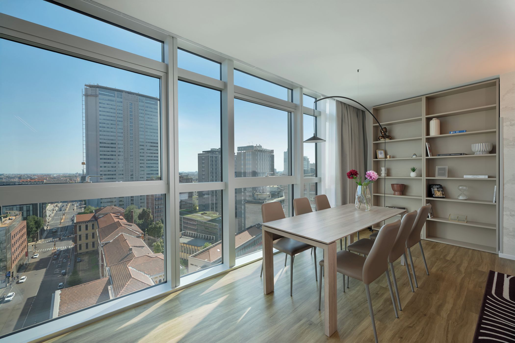 A modern apartment with a large balcony, a dining area with a table and chairs, and a bookshelf.