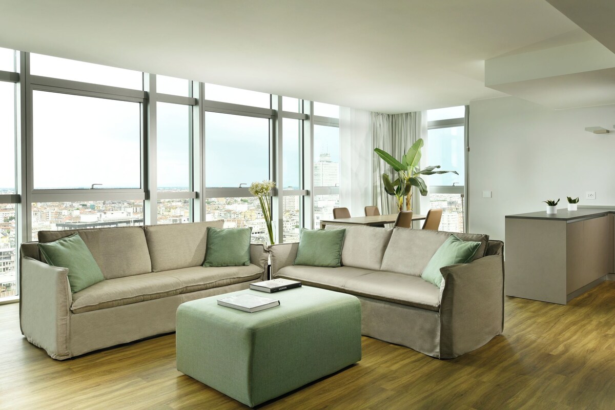 A modern living room with a sectional sofa, a small ottoman, and a dining area with a table and chairs.