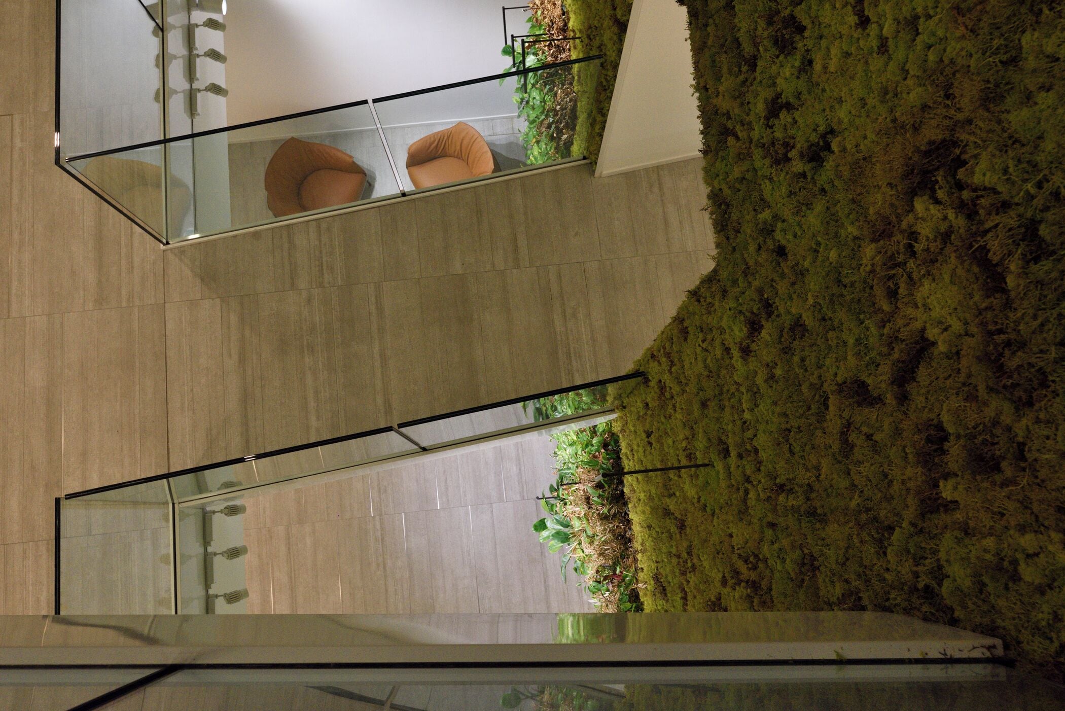 A modern interior with a glass partition, a seating area with cushions, and a green wall with plants.