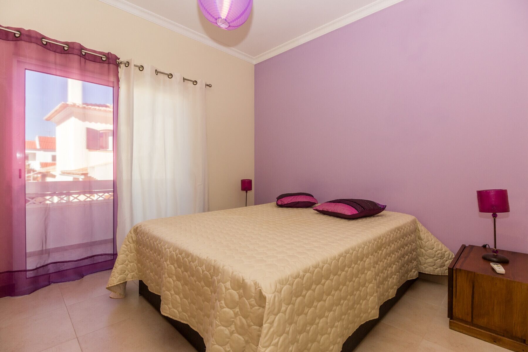 Un dormitorio con cama, cortinas, mesita de noche y lámpara.