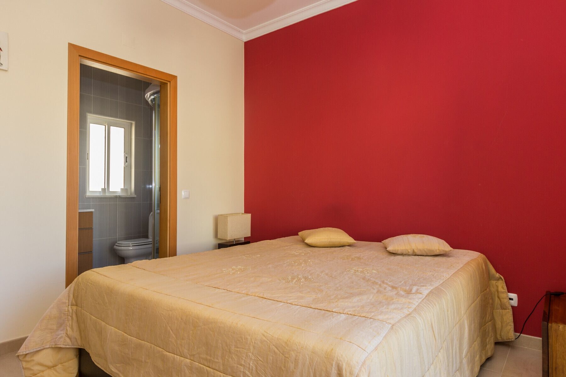 A bedroom with a bed, a nightstand, a lamp, and a red wall.