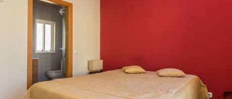 A bedroom with a bed, a nightstand, a lamp, and a red wall.