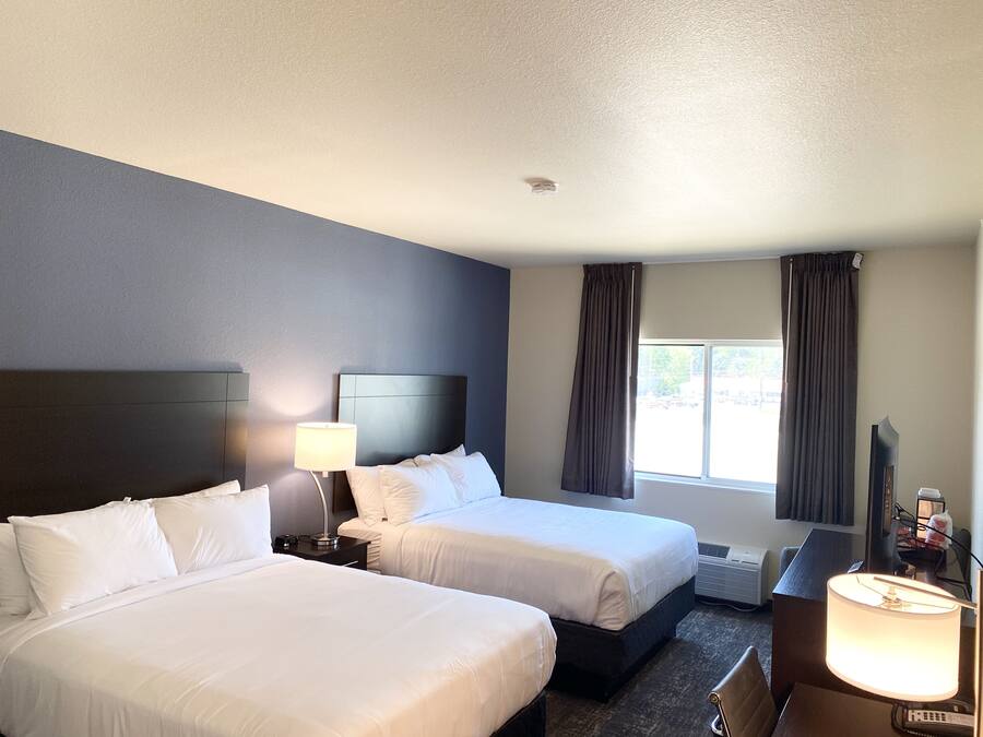 A hotel room with two beds, a desk, a chair, a lamp, and a window with curtains.