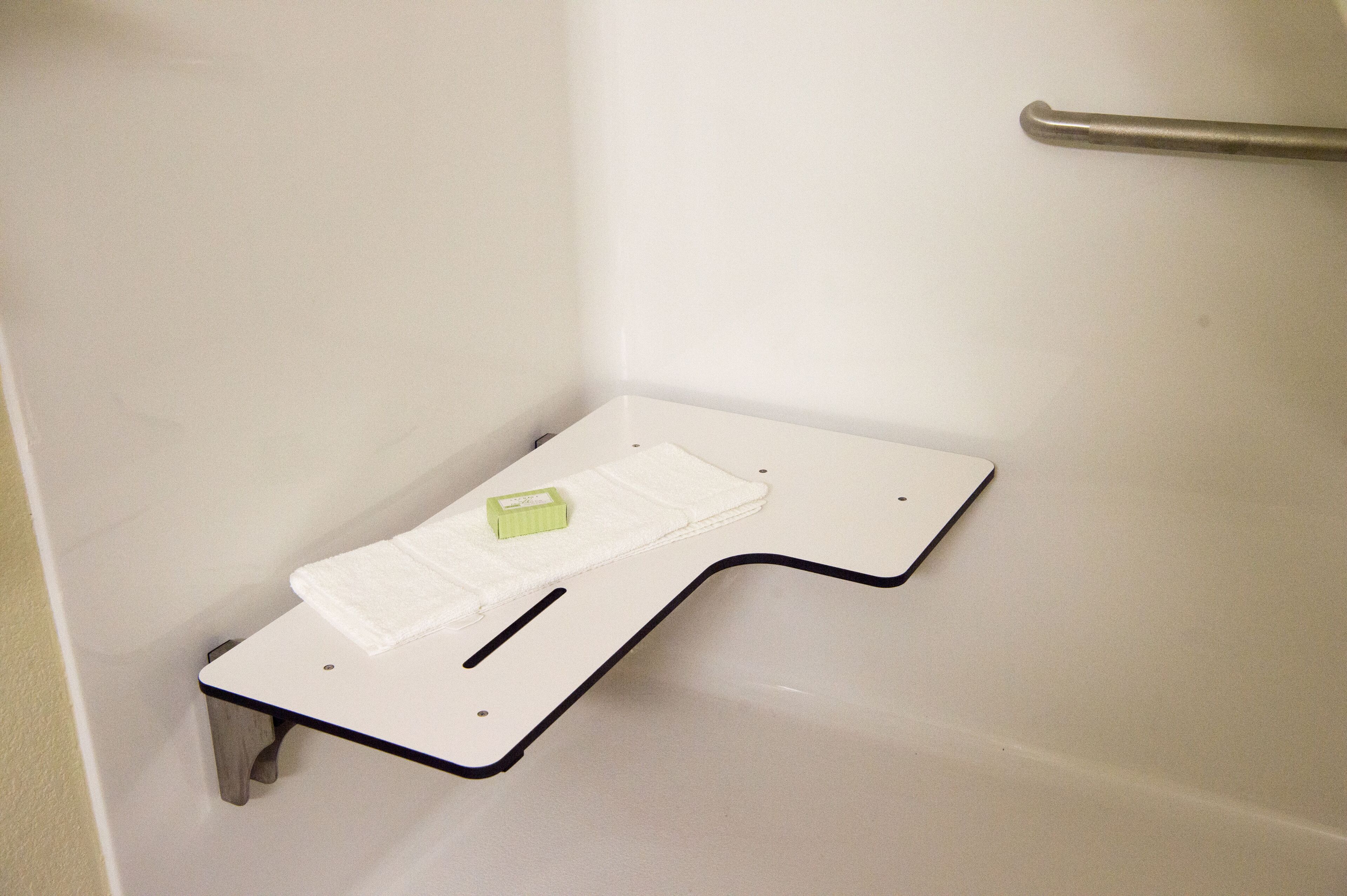 Eine weiße Badewanne mit eingebautem Ablagefach, ein weißes Handtuch und eine grüne Seife.