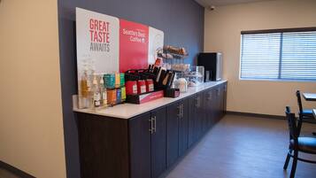 Uma área de recepção com um balcão exibindo café e bebidas, um letreiro grande com a inscrição "Seattle's Best Coffee" e uma janela com persianas.