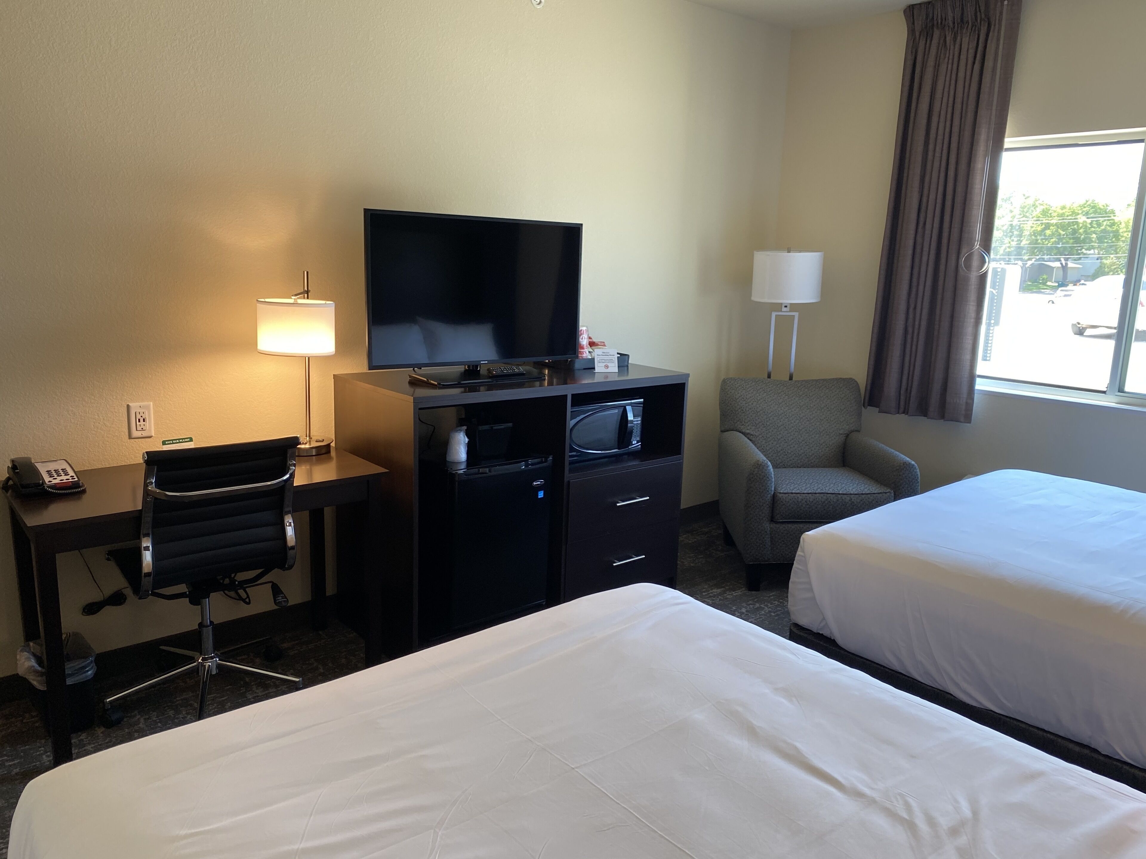 A hotel room with a desk, a television, a chair, and two beds.