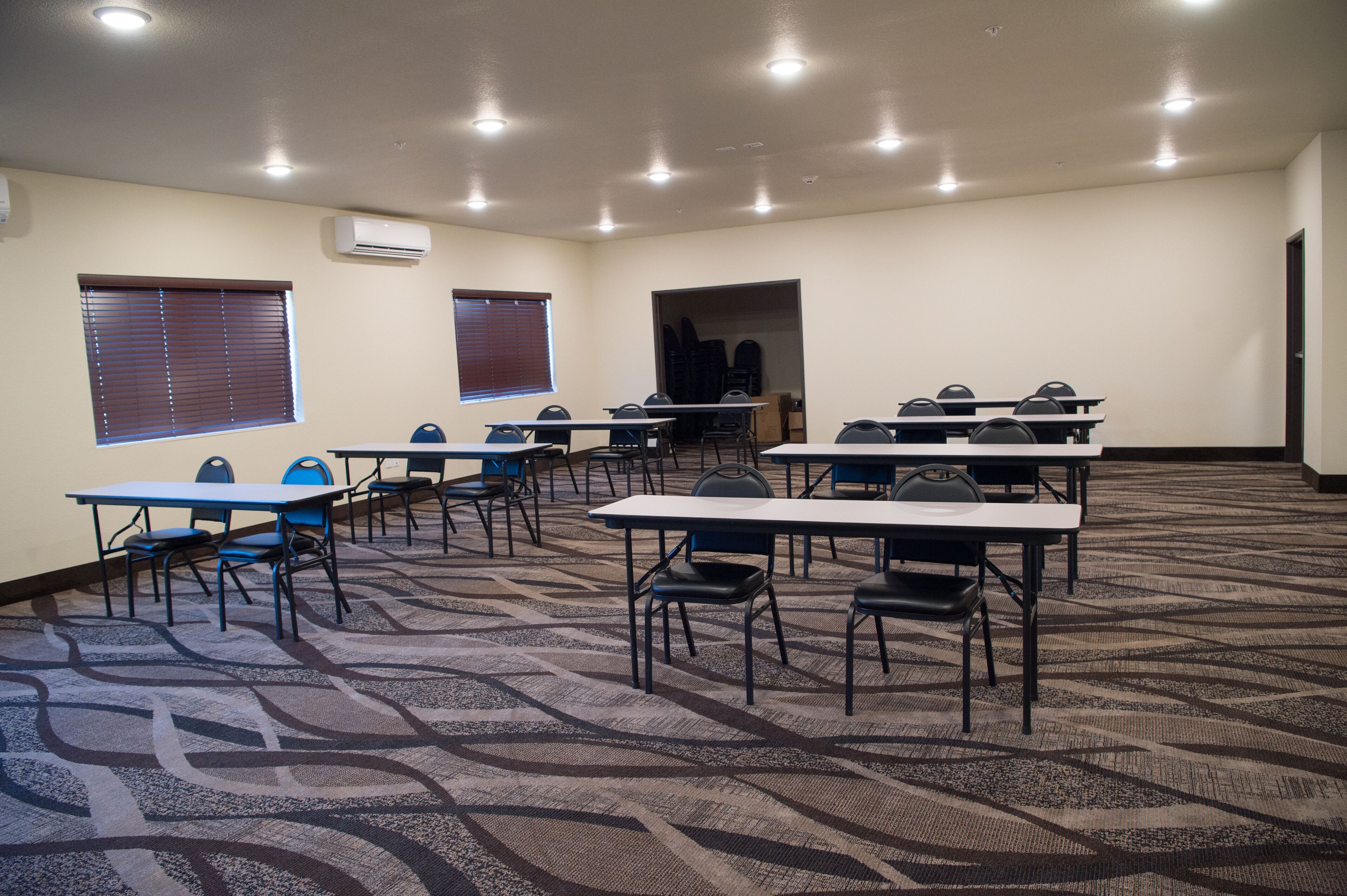 Una sala conferenze con diversi tavoli e sedie, pavimento in moquette e luci a soffitto.