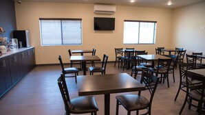 Un comedor con varias mesas y sillas, un televisor de pantalla plana montado en la pared y una ventana con persianas.