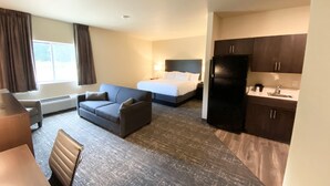 Habitación de hotel con cama, sofá, escritorio, silla, refrigerador y kitchenette.