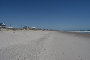 A wide sandy beach with footprints, a clear blue sky, and houses in the background. - Ocean & Sound Views; 2 King Suites; Elevator (Surf City)