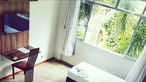 Un dormitorio pequeño y ordenado con escritorio, cama y ventana con vistas a zonas verdes.