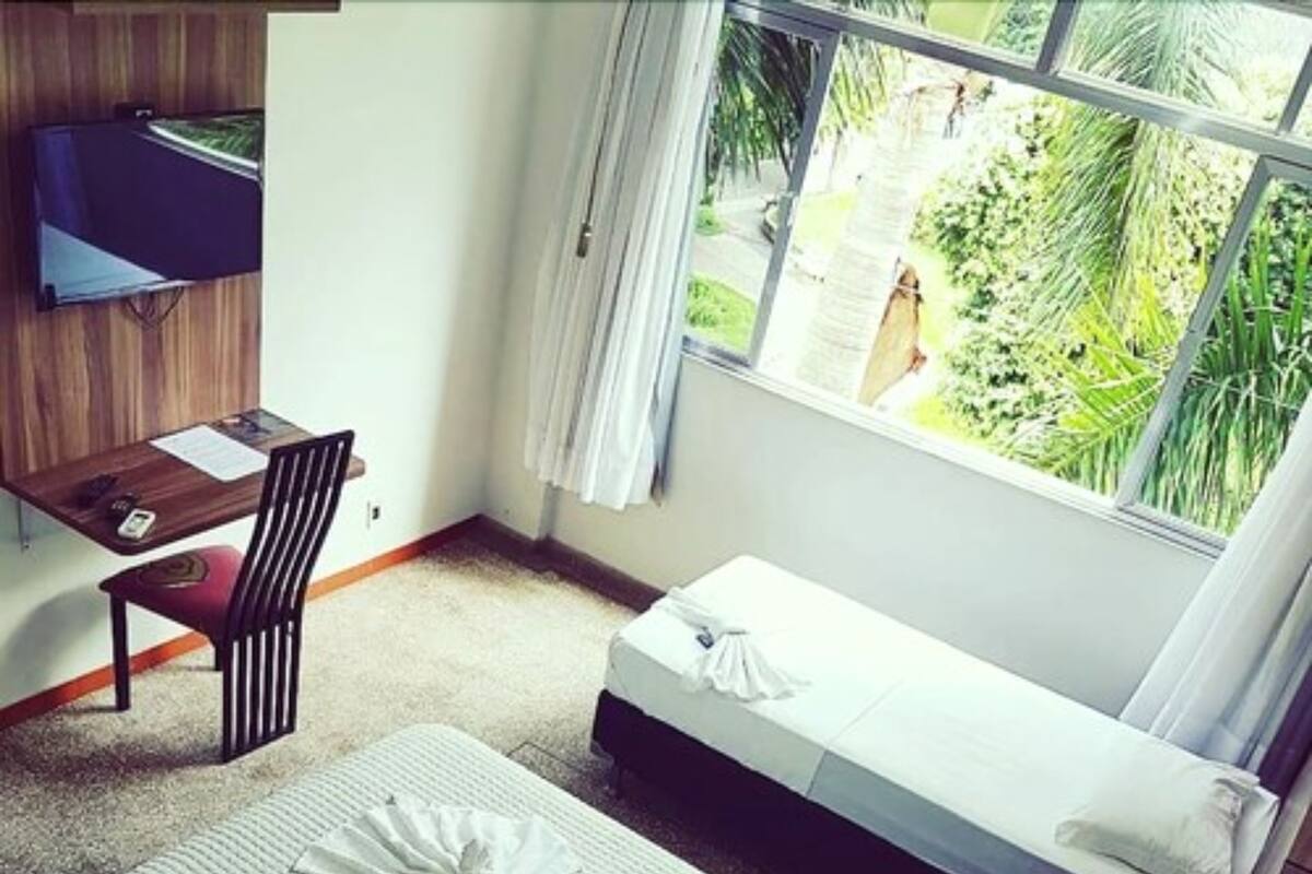 A small, neatly arranged bedroom with a desk, a bed, and a window with a view of greenery.