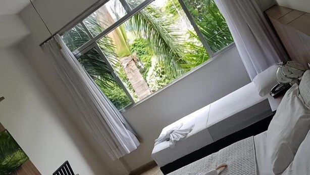 Habitación de hotel con cama, una silla, un escritorio y ventana con vistas a zonas verdes.
