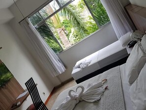 A hotel room with a bed, a chair, a desk, and a window with a view of greenery. - Hotel Imperial De Carangola (Carangola)