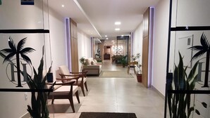 Un vestíbulo de hotel con mostrador de recepción, zona de estar y plantas en macetas.