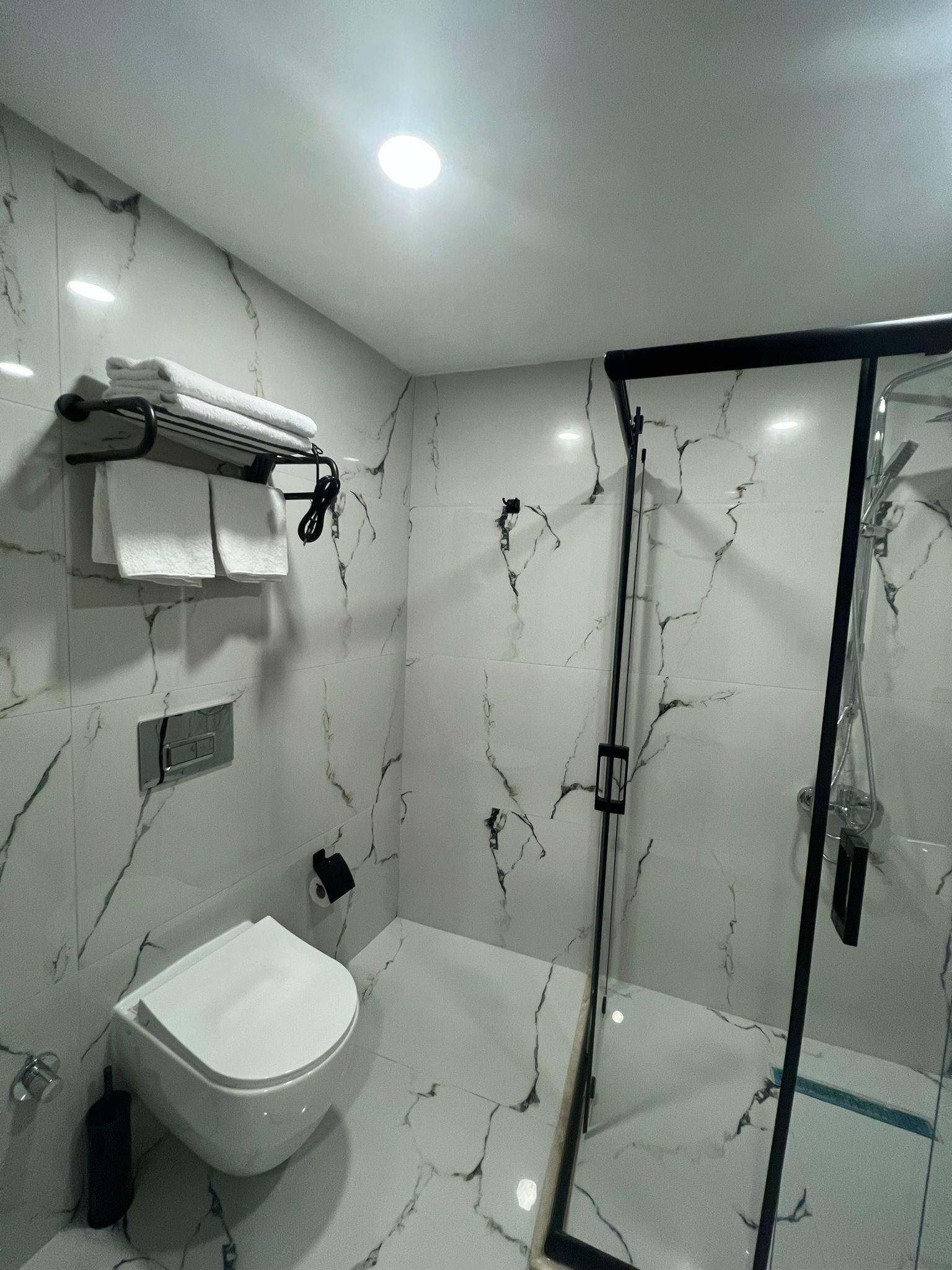 A modern bathroom with a white marble backsplash, a glass-enclosed shower, and a white toilet.