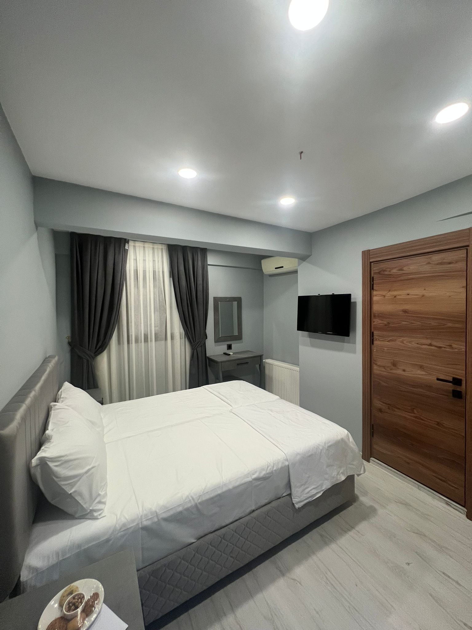 Une chambre à coucher comprenant un lit, une table de chevet, un miroir, une télévision et une armoire en bois.
