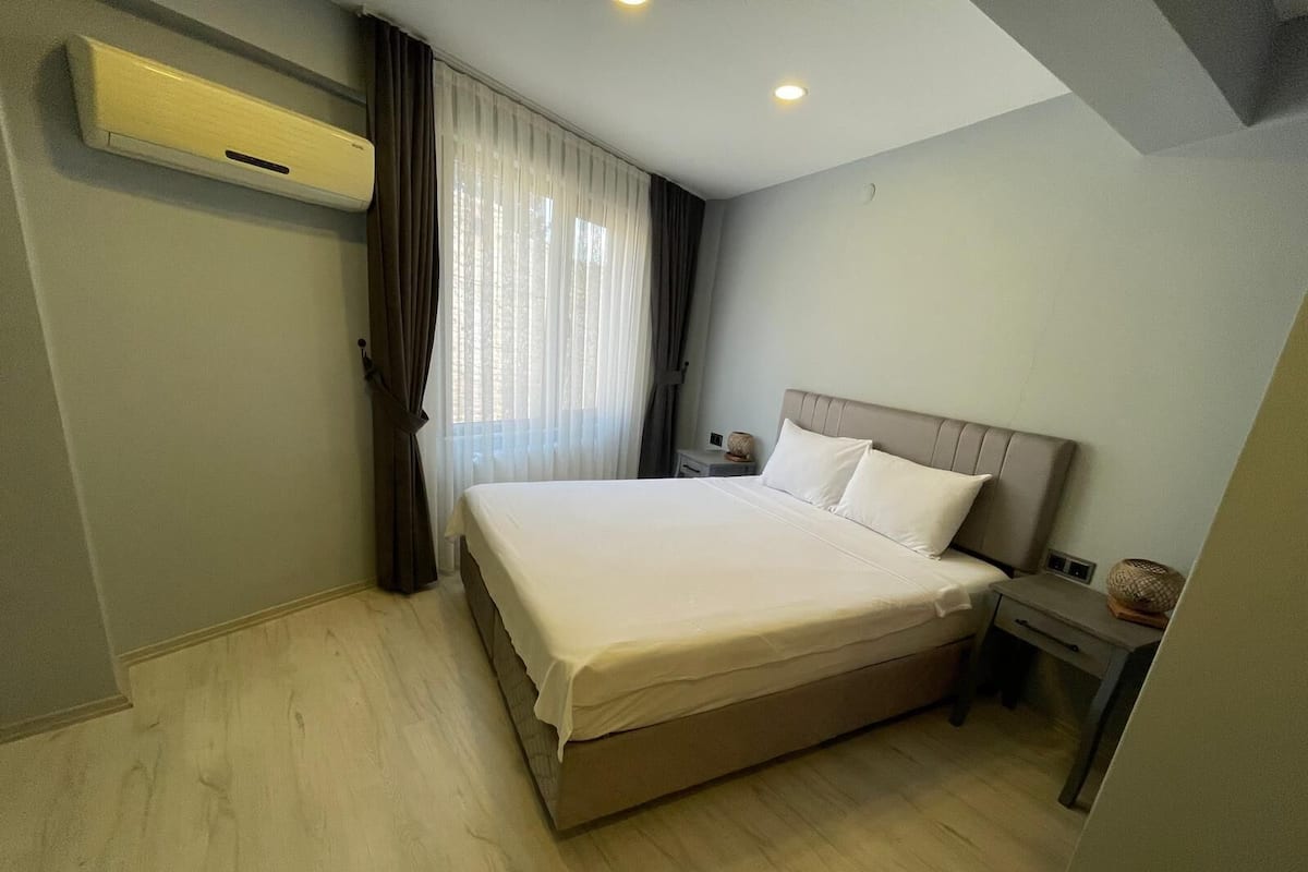 A modern hotel room with a large bed, a bedside table, a nightstand, and a window with curtains.