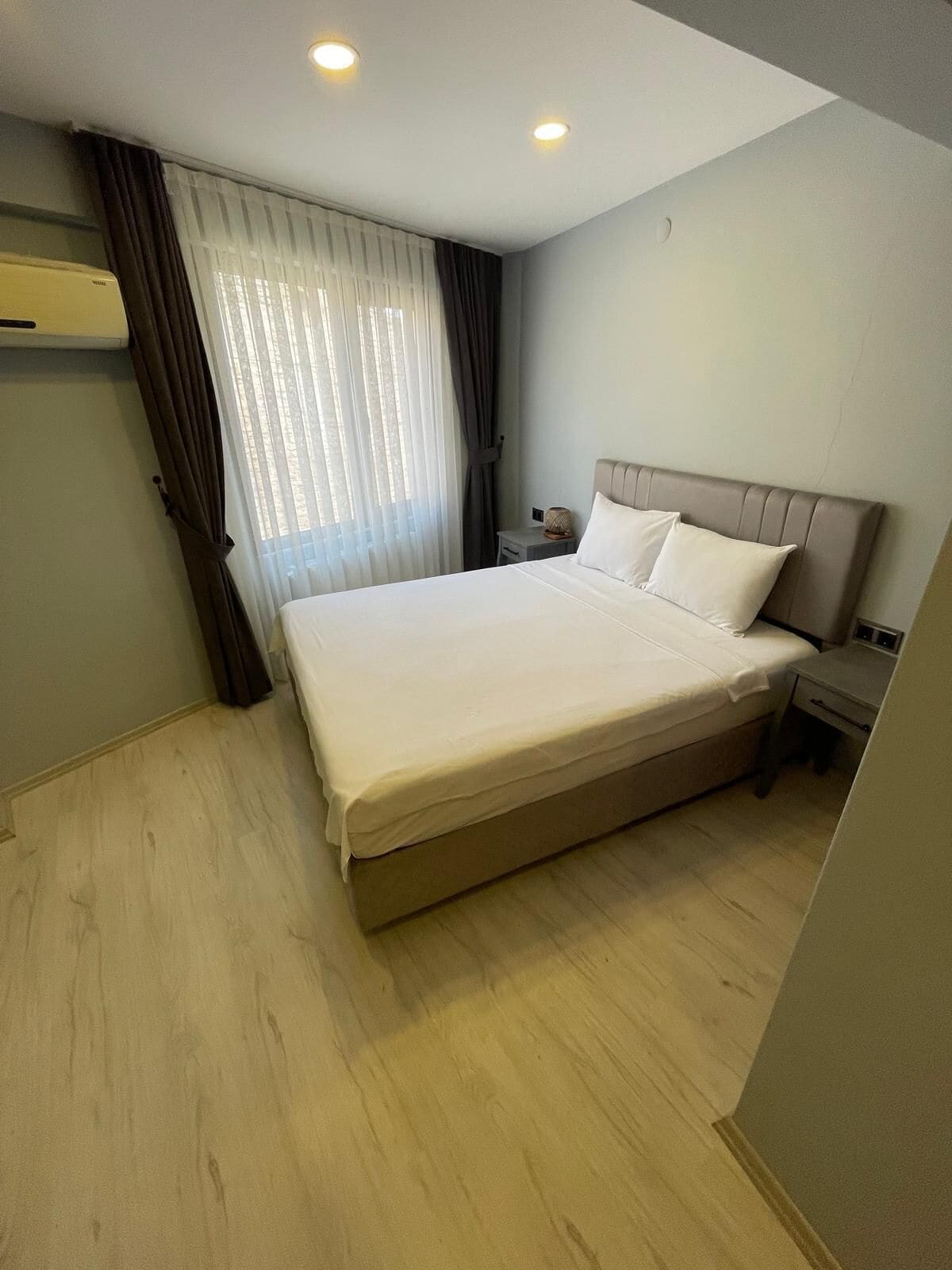 A hotel room with a large bed, a nightstand, a lamp, and a window with curtains.