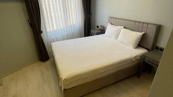 A hotel room with a large bed, a nightstand, a lamp, and a window with curtains.