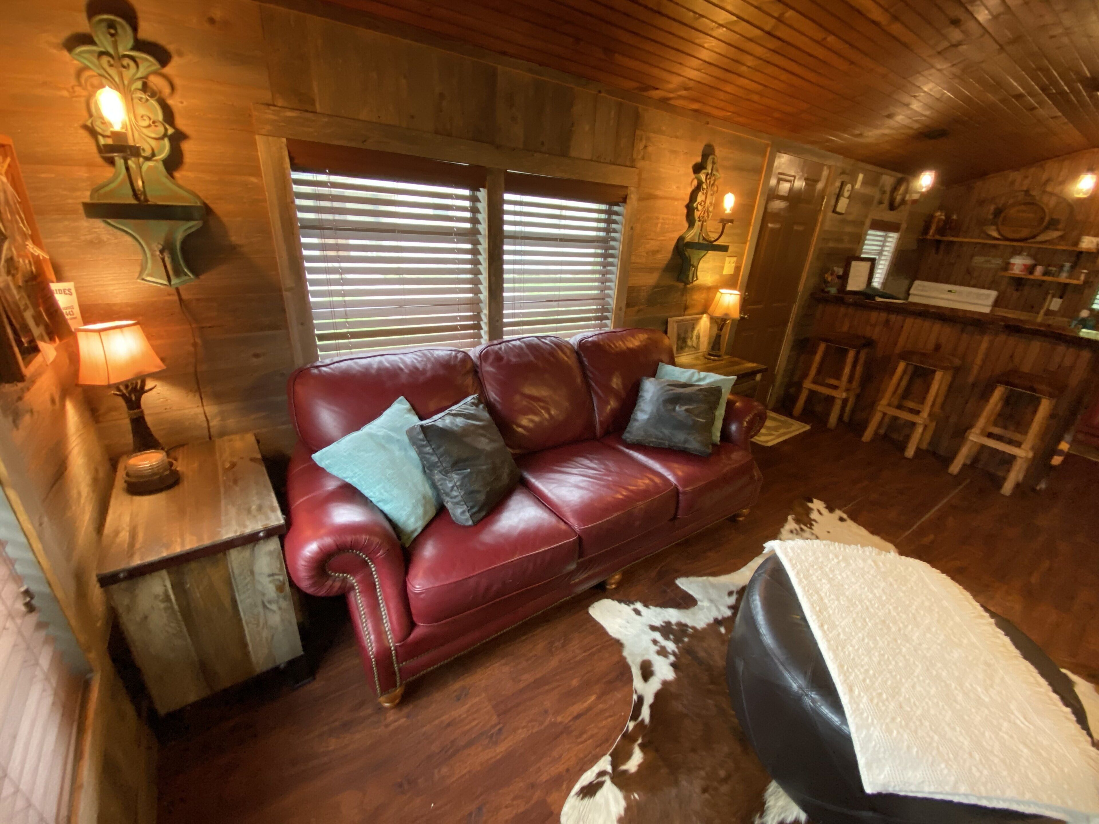 A cozy room with a red leather sofa, wooden walls, and a bar area.