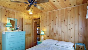 A wooden-paneled room with a bed, dresser, and ceiling fan. - The Boathouse Cottage is a beachfront family retreat (Saco)