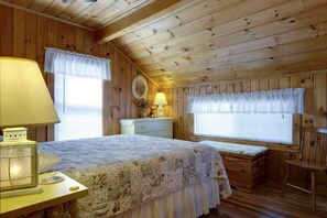 Un dormitorio tipo cabaña acogedor con cama, cómoda, tocador y una silla.