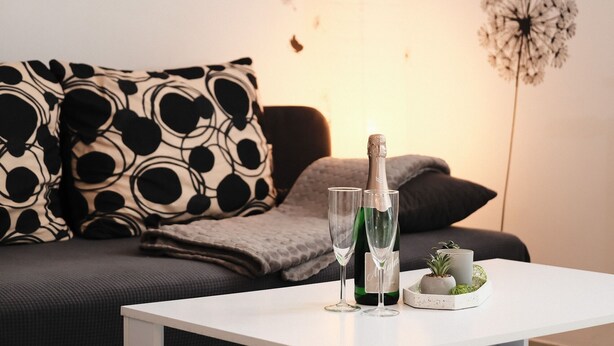 A living room with a white table, a bottle of champagne, two glasses, and a decorative plant on the table. - Apartment mit Wohnflair (Essen)