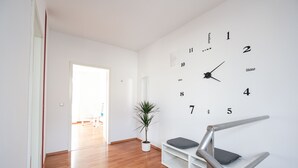 A modern interior with a wooden floor, a white wall clock, a potted plant, and a staircase with a metal railing. - Apartment mit Wohnflair (Essen)