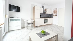 A modern kitchen with white cabinetry, a built-in oven, and a flat-screen TV mounted on the wall. - Apartment mit Wohnflair (Essen)