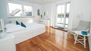 A modern bedroom with a bed, bedside table, chair, and a view of the outside through a large window. - Apartment mit Wohnflair (Essen)
