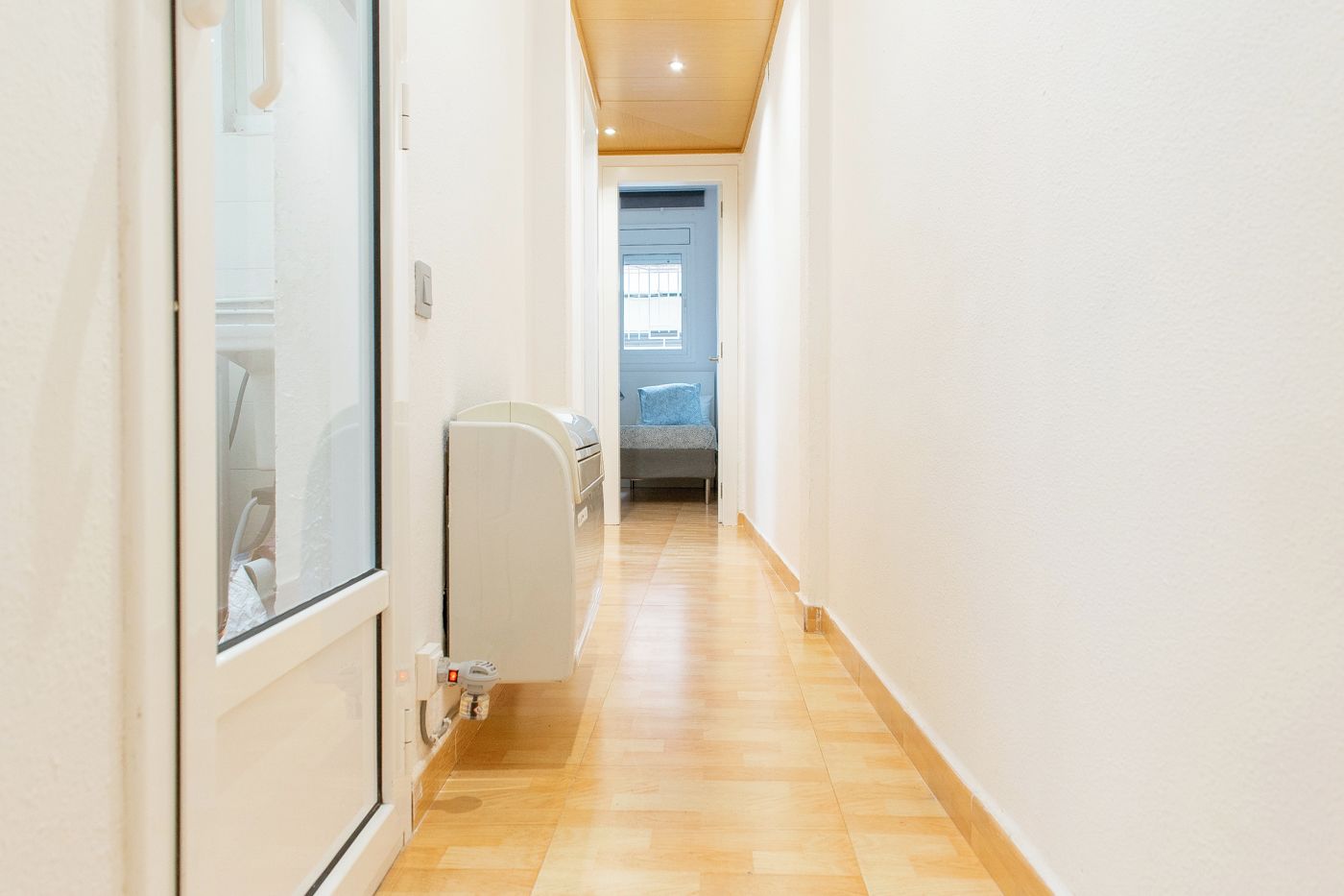 A narrow hallway with a radiator, a door, and a window at the end.