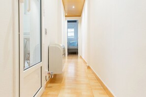 Een smalle gang met een radiator, een deur en een raam aan het einde.