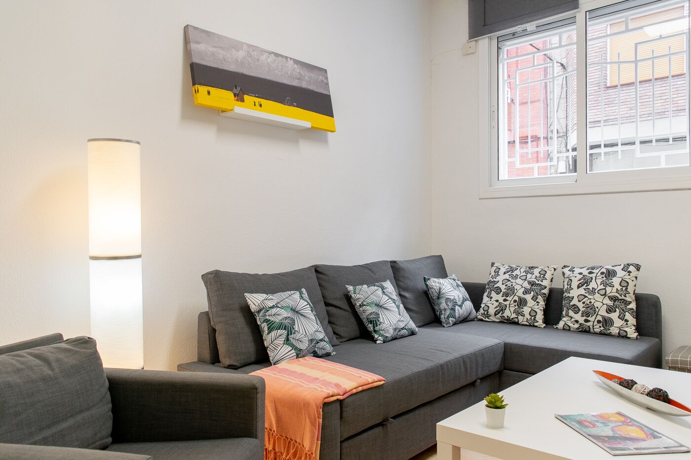 En moderne stue med en grå hjørnesofa, et hvidt sofabord og et billede over sofaen.