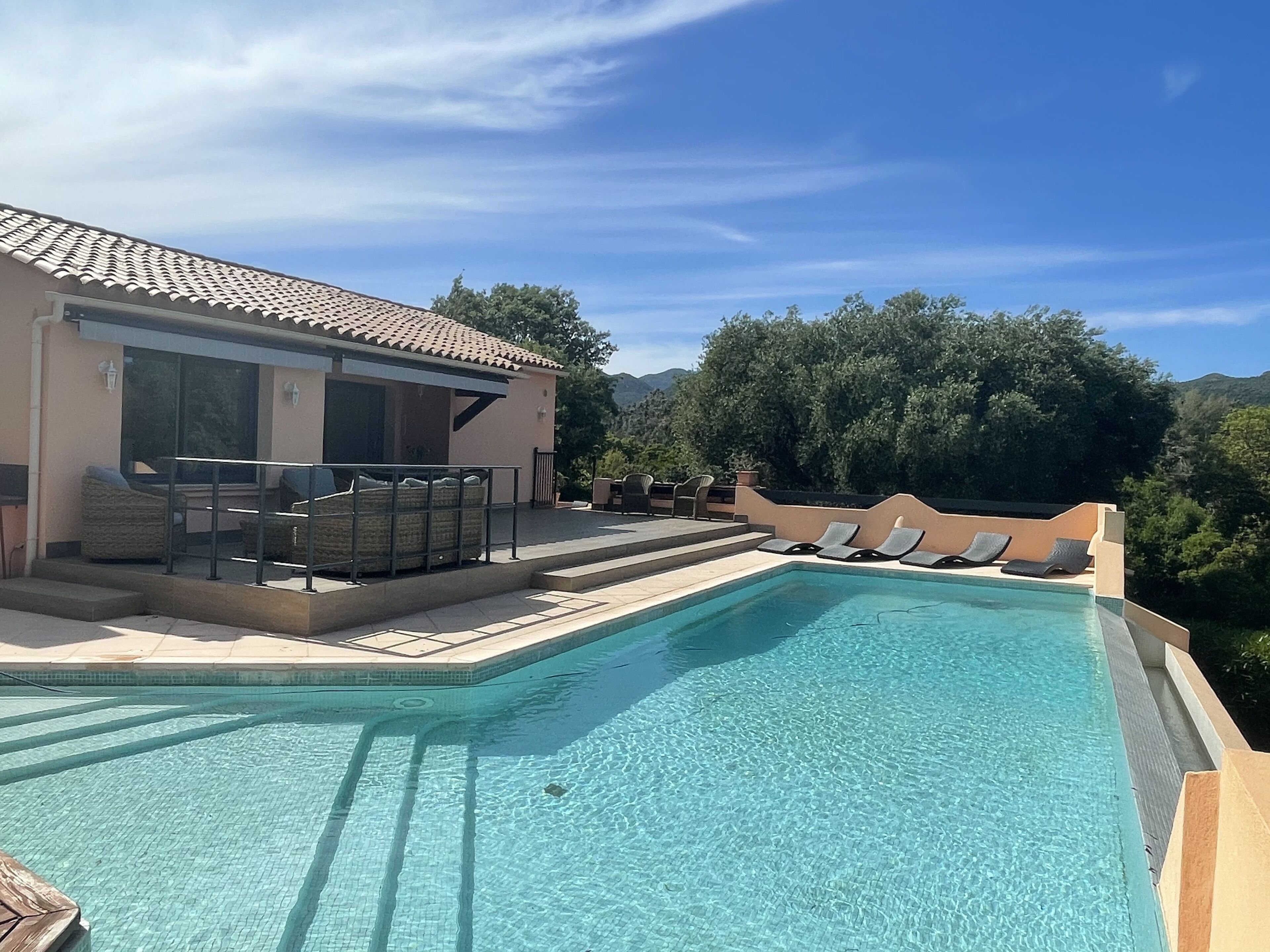 A swimming pool with lounge chairs, a covered seating area, and a building with a tiled roof.