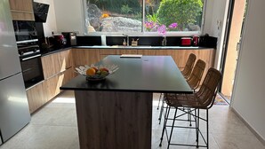 A modern kitchen with a central island, wooden cabinets, and a view of greenery outside.