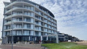 A multi-story hotel with a curved facade, outdoor seating, and a well-maintained lawn. - 32  Bay View Suites  (Langstrand)