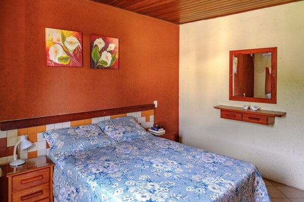 A bedroom with a bed, nightstand, lamp, and two paintings on the wall. - Villa Oliva Residence (Florianópolis)