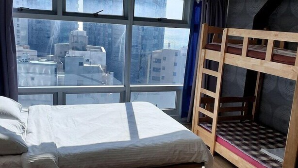 Una stanza con un letto a castello, un'ampia finestra vista città e un letto con lenzuola bianche.