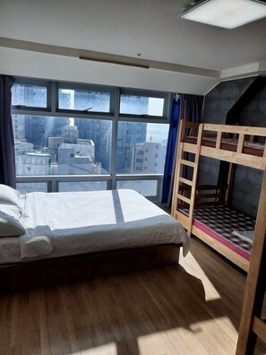 A room with a bunk bed, a large window with a city view, and a bed with white linens. - Popcorn Hostel Haeundae (Busan)