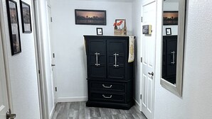 Un couloir doté d’un plancher en bois, d’un meuble de rangement noir et d’un miroir sur le mur de droite.