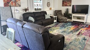 Un salon comprenant un canapé d’angle, un tapis à motifs, un téléviseur et des objets décoratifs.