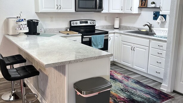 Une cuisine moderne avec des meubles blancs, un four à micro-ondes en acier inoxydable, une cuisinière noire et un coin bar avec deux tabourets.