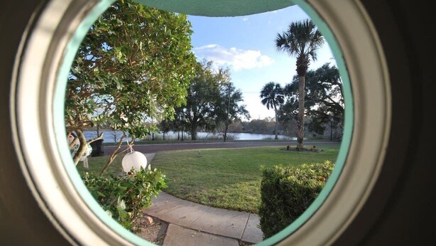 A view through a window of a park with a lawn, trees, and a body of water. - Lakefront - Lake Davis Art Deco Cottage (Orlando)