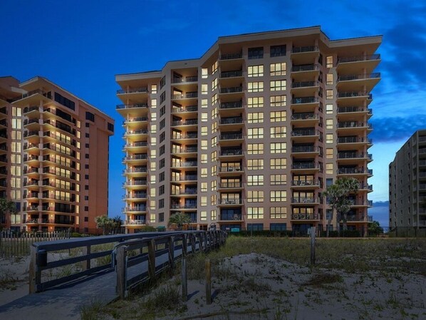 Un hôtel à plusieurs étages doté de balcons, offrant une vue sur la plage et donnant sur une étendue de sable.