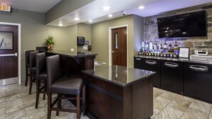 A bar area with a counter, seating, a TV mounted on a stone wall, and a variety of bottles. - Cobblestone Inn & Suites - Brookville (Brookville)