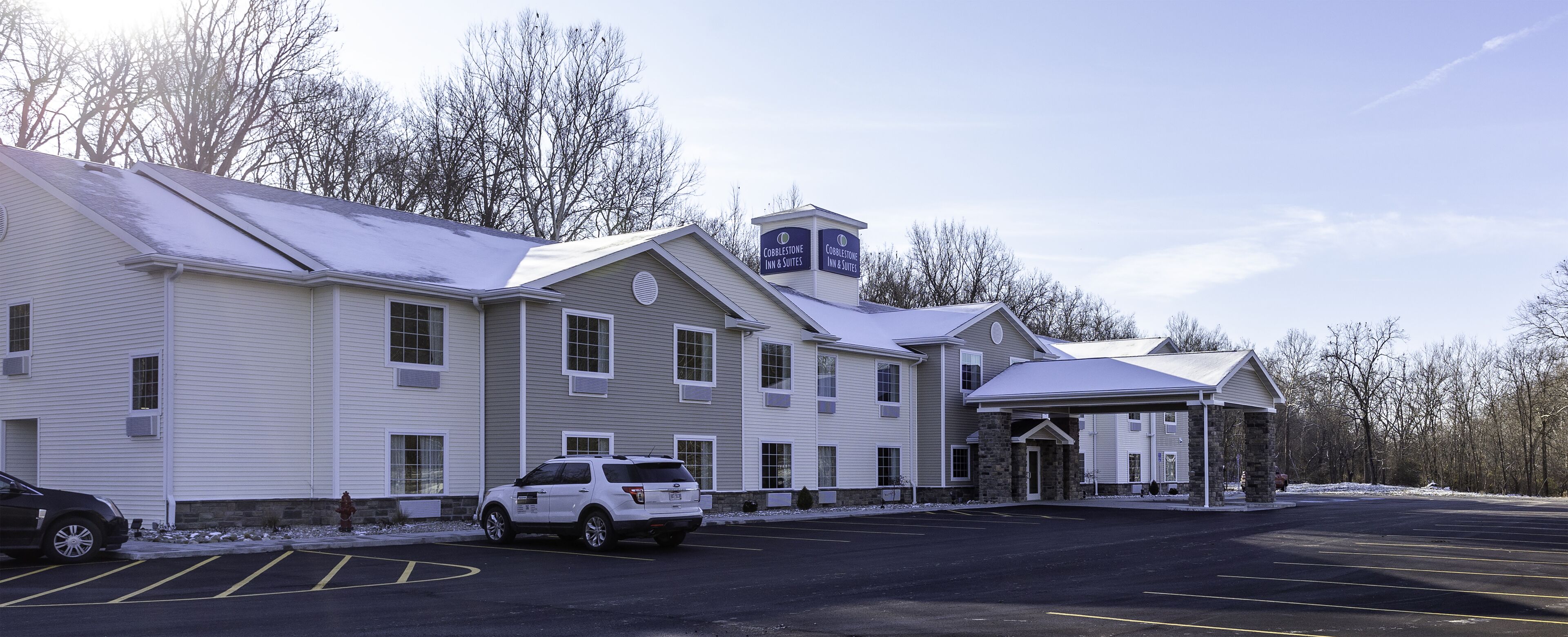 A Cobblestone Inn & Suites with a covered parking area and a snow-covered landscape.